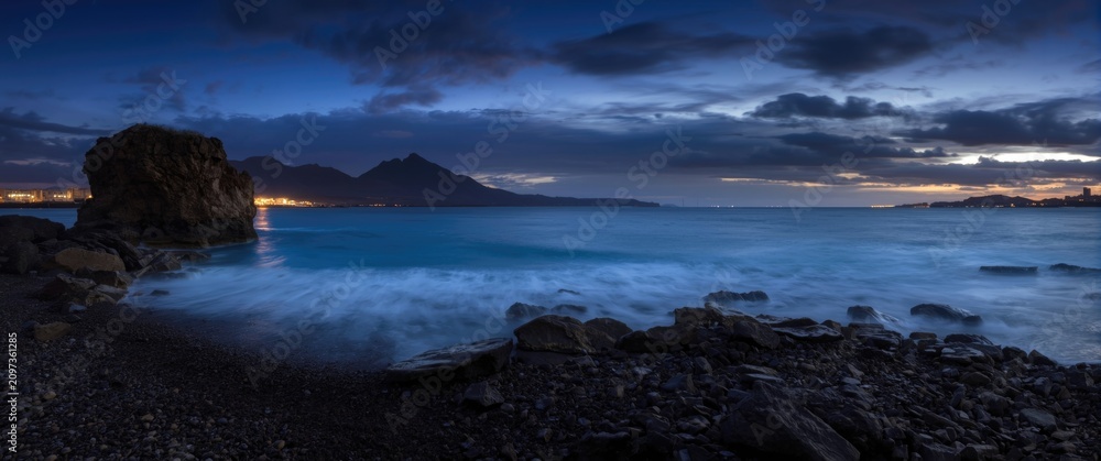 Fototapeta premium Seascape at Dusk with Mountains and Soft Waves on Rocky Shore