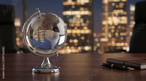 Crystal glass globe on a wooden office desk with a fountain pen and notebook against a blurred city night skyline