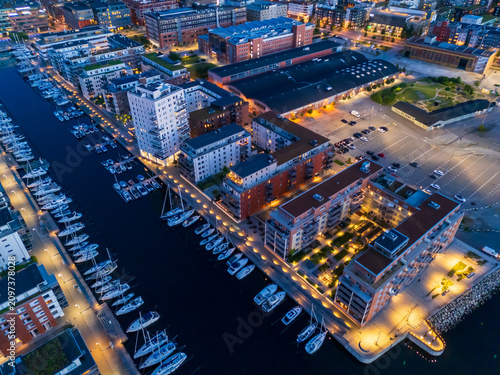 Aerial drone view over Malmö harbor during blue hour, summer twilight, showcasing vibrant city skyline, shimmering water, and peaceful Scandinavian atmosphere with professional composition.