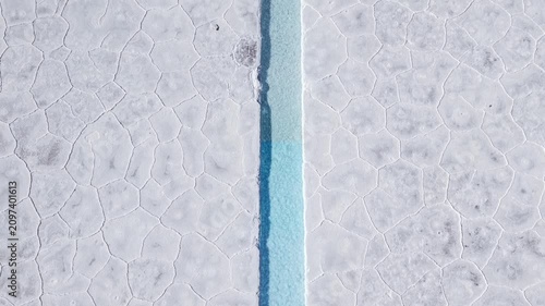 Drone aerial video of turquoise salt channels and white salt flat rows in Salinas Grandes, Argentina.
