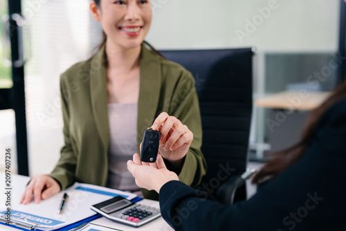 Happy female client receives car key and money from financial agent after auto loan approval. Finance, vehicle purchase, banking, trust, success, and ownership concept.