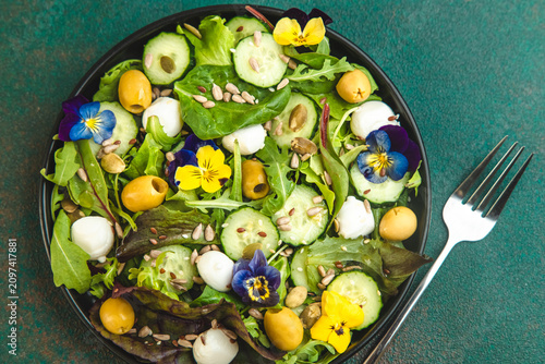 Foto Fresh salad with greens cucumbers olives and edible flowers served on a black pl