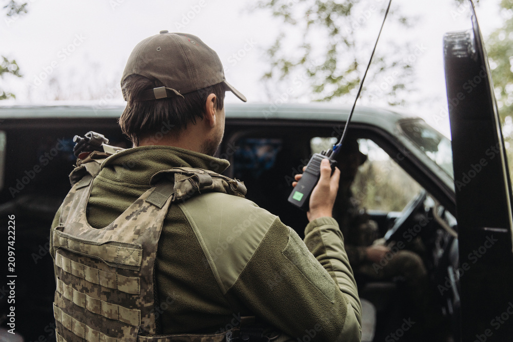 Fototapeta premium Ukrainian soldier communicating by radio near military vehicle