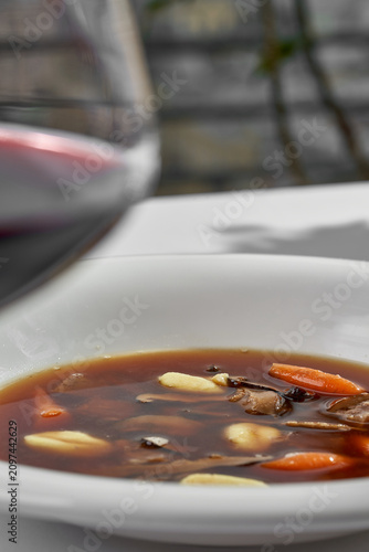 Gourmet mushroom broth soup with gnocchi and baby carrots on a white plate. Minimalist top view fine dining table setting with hard shadows.