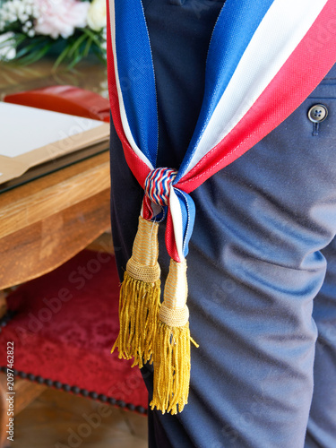 Écharpe tricolore à franges dorées portée par un maire français lors d'une cérémonie officielle en mairie