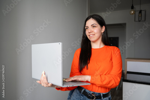 Young woman holding laptop in home office environment smiling confidently. Remote work online presentation and digital productivity