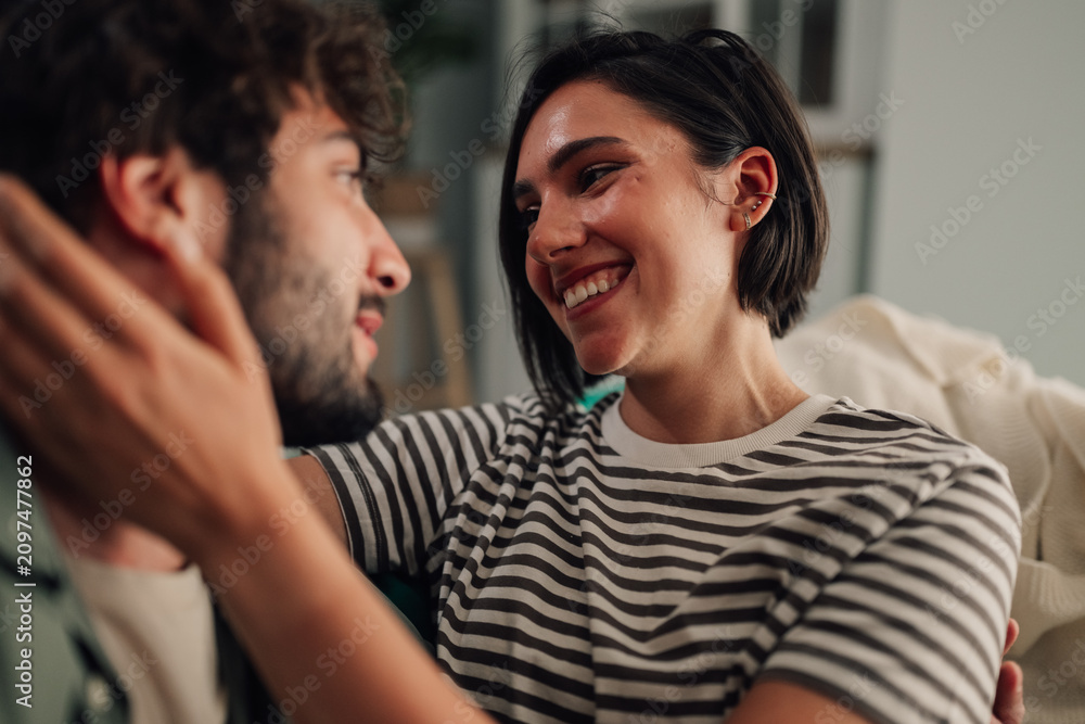 Obraz premium Cheerful couple embracing, touching face, expressing love and trust in a cozy home setting, enjoying their relationship