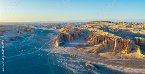Aerial view of unique geological yardang landforms with dry clay cliffs in a vast arid desert at sunset, Dahaidao, Xinjiang, China