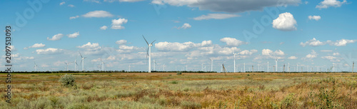 Wind turbine in a field generating clean renewable green energy under a blue sky with clouds.