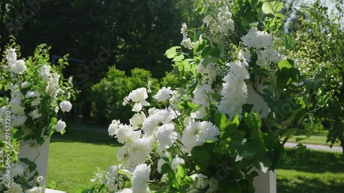 Beautiful white floral arrangements with greenery create a stunning backdrop in a garden, enhancing the romantic atmosphere for a wedding ceremony