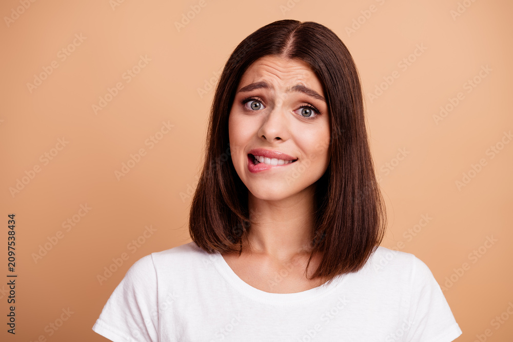 Fototapeta premium Brunette young woman in white tshirt making a funny awkward expression against beige background