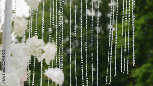 Beautiful wedding ceremony decoration featuring white flowers and hanging crystal beads, creating a romantic atmosphere in an outdoor setting