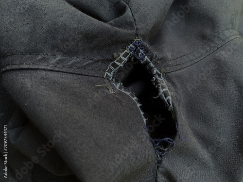 Photography Close up of a ripped hole on the seam of black fabric pants.