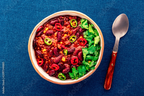 Spicy chili con carne, traditional Mexican beef stew. Flat lay on blue background