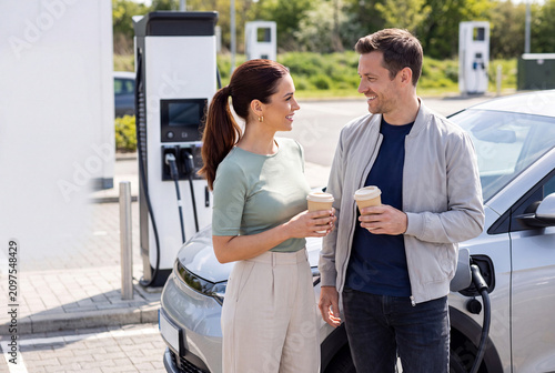 Happy couple near electric car charging station enjoying sustainable modern lifestyle