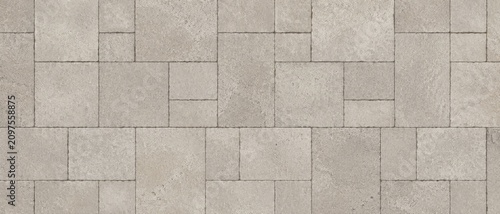 Overhead view of beige rectangular concrete pavers arranged in an interlocking geometric pattern across paved patio or walkway surface with textured finish and visible grout lines