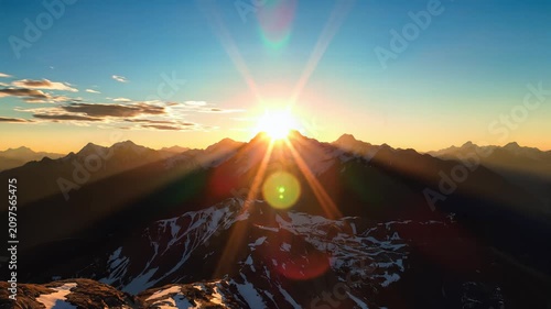Golden sunrise illuminating rugged snowy mountain peaks with dramatic sky and lens flare