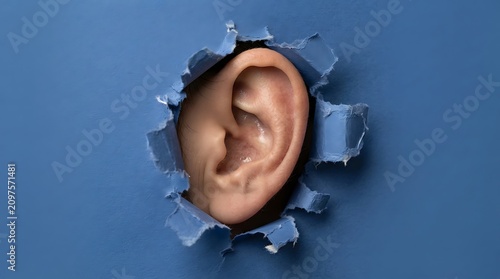 Human ear peeking through a hole in a blue paper background