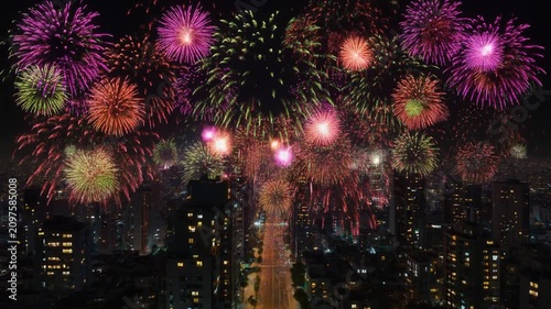Vibrant multi-colored fireworks exploding above a dense urban cityscape during a festive night celebration