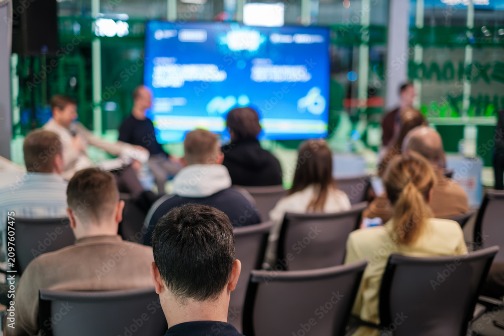 Obraz premium Business audience seated watching blurred presentation screen at conference, networking, learning atmosphere, modern meeting space.