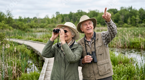 Elderly couple enjoying birdwatching on a boardwalk in a wetland nature preserve