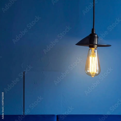 A dimly lit room with a single light bulb hanging from a black cord against a blue wall, illuminating a portion of it
