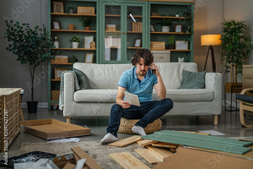 Foto Frustrated man assembling flat pack furniture calling for help