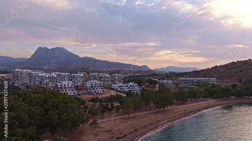 Footage shows a coastal area at sunset with buildings and mountains in the distance. The beach is empty and the sky has many colors as the sun sets behind the mountains.