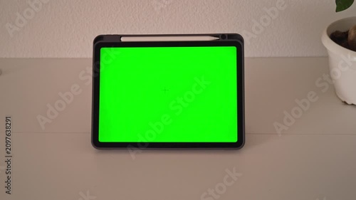 The tablet is placed on a table with a green screen showing across the display. The camera captures different angles and focuses. A small plant is in the background.