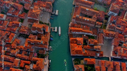 Top down aerial view of the Grand Canal in Venice, Italy, with a vaporetto water bus, work boats, a ferry pontoon, moored boats and terracotta rooftops lining both banks in spring.