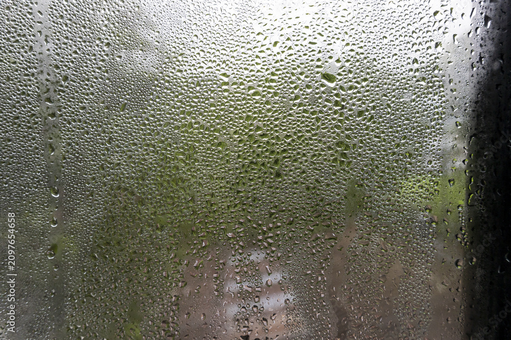 Obraz premium Dew drops on glass window with blurred green foliage outside creating moody atmosphere, closeup texture and condensation pattern