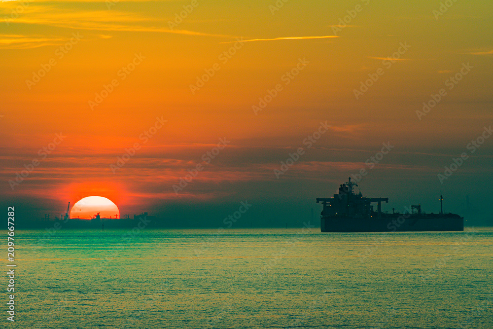 Naklejka premium Cargo ship sailing at sunset in industrial port
