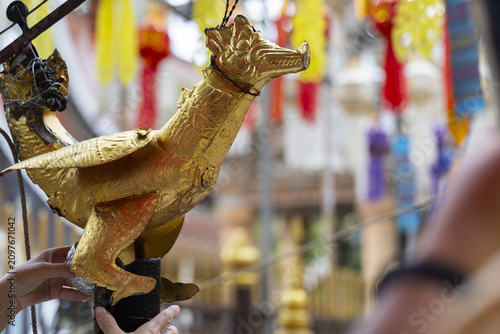 Quadro su tela Golden mythical bird sculpture at temple celebration with blurred colorful flags