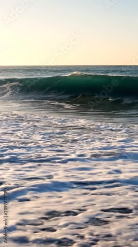 Ocean waves crashing on sandy beach during golden sunset.