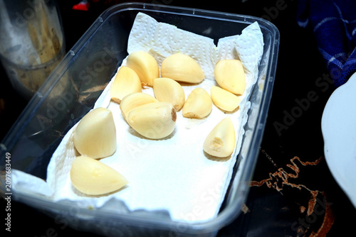 clear plastic container lined with a white paper towel, holding several clean, peeled white garlic cloves ready for cooking.
