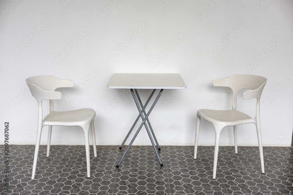 Obraz premium Minimalist white chairs and compact table on patterned tile floor creating modern calm seating scene with soft light and clean lines
