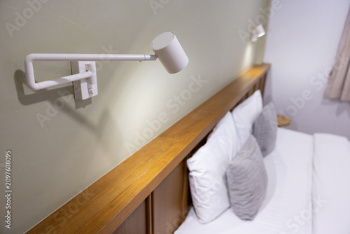 Quadro su tela Modern bedside reading lamp over wooden headboard and neatly made bed with white
