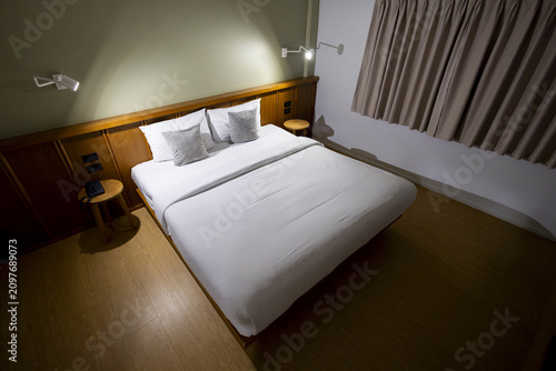 Quadro su tela Modern hotel room bed with white linens and pillows under bedside lamps, warm wo