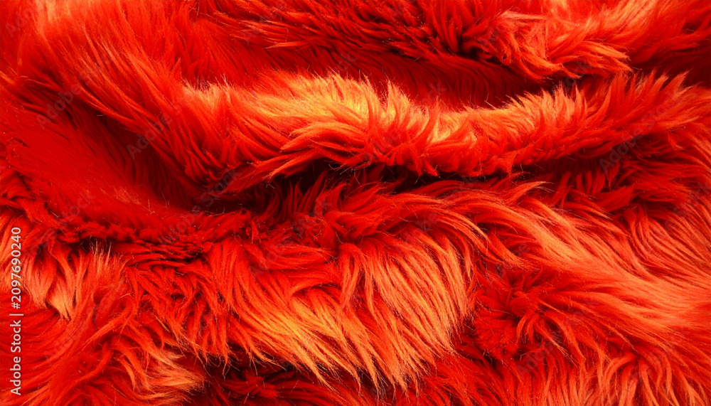 Fototapeta premium Close-up of vibrant orange-red shaggy faux fur fabric with a deep, irregular pile, showcasing intricate texture and soft folds under warm, dynamic lighting.