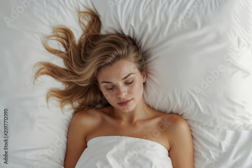 Top view of beautiful woman sleeping in bed with her hair down on white sheets