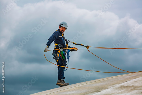 Male worker rope access industrial working at height tank oil wearing harness, helmet safety equipment rope access inspection of thickness