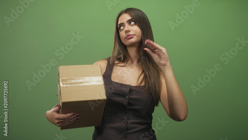 Fotografie Woman holding cardboard box with one hand and hand raised in a dismissive flick gesture in studio; indifference delivery logistics