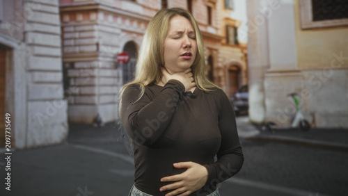 Foto Woman grasping throat with one hand and pressing her stomach while choking on a cobbled street; panic emergency help