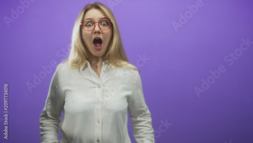 Принти на полотні Woman wearing red glasses with mouth open in surprise and hands mid motion, white blouse, studio purple backdrop; surprise celebration