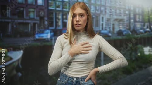 Fotografía Woman hand on chest in a touching pose on a city street with boats and row buildings nearby; sincerity reflection