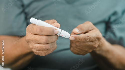 Bilde på lerret Close-up of a senior adult using a lancet device for finger prick blood glucose testing at home