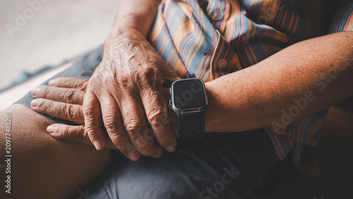 Close-up of senior hands resting on a lap while wearing a smartwatch, representing healthy aging, wearable healthcare technology, wellness monitoring, independent living, preventive care.
