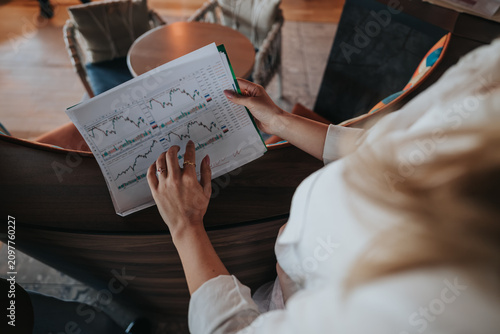 Fotografie A businesswoman studies printed stock charts and market data while seated in a casual office