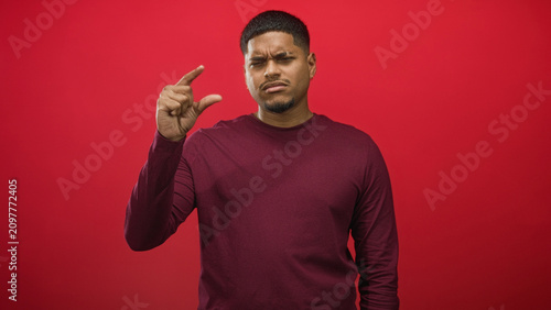 Картината върху платно Man pinching thumb and forefinger to show a small distance against a red studio wall, frowning while holding hand forward; doubt small size