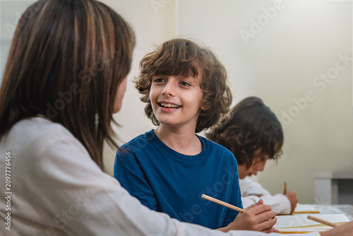 Konstfotografi Smiling boy pupil discussing with young girl classmate during handwriting lesson
